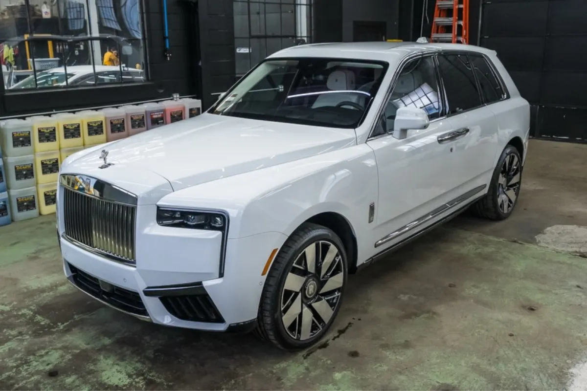 Front angle of white Rolls Royce SUV in shop with polished exterior and reflections