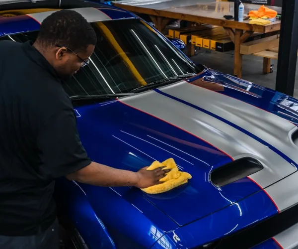 Technician polishing blue Dodge Challenger during car detailing.